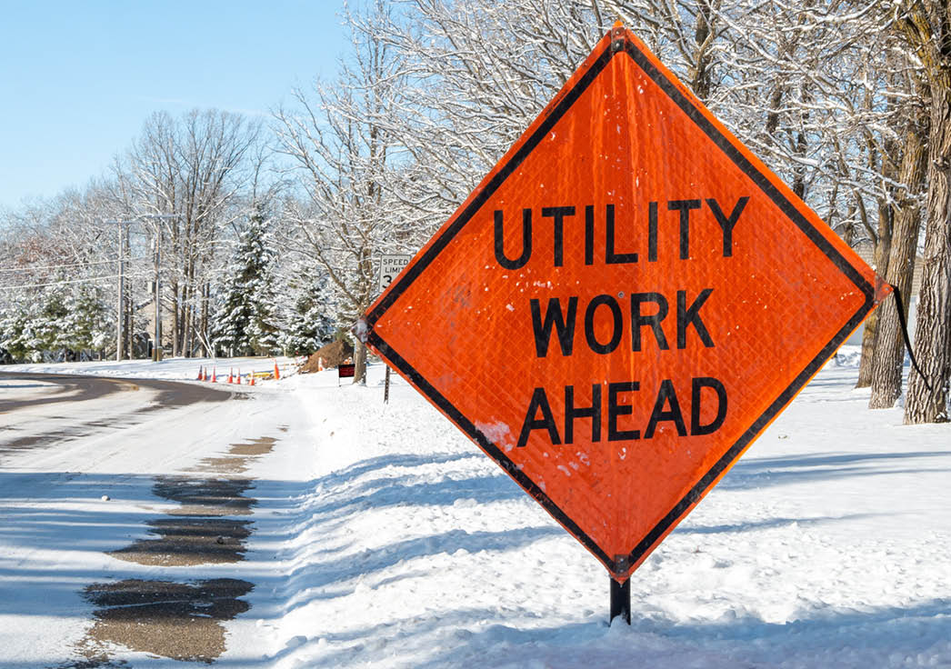 Orange UTILITY WORK AHEAD sign warns traffic about a work zone on a snowy city street, on a frosty and sunny winter day in Bemidji, Minnesota.