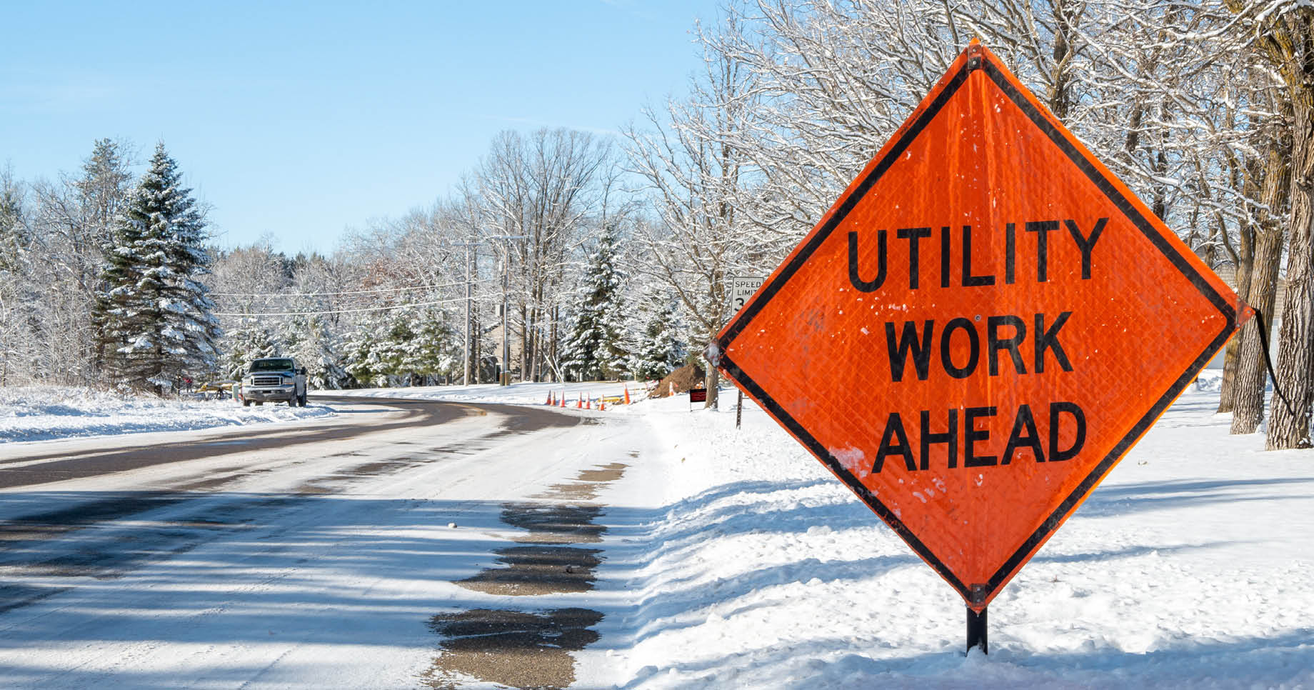 Orange UTILITY WORK AHEAD sign warns traffic about a work zone on a snowy city street, on a frosty and sunny winter day in Bemidji, Minnesota.